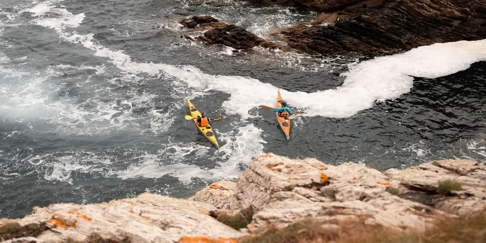 Due kayak pagaiano lungo una costa rocciosa