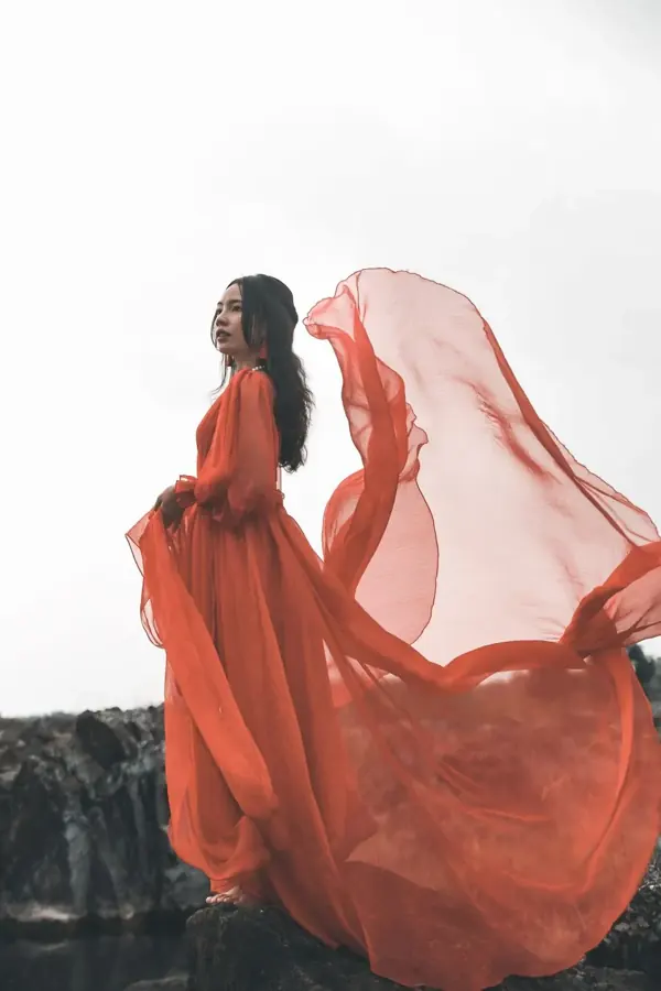 Donna in abito rosso fluttuante sulla scogliera